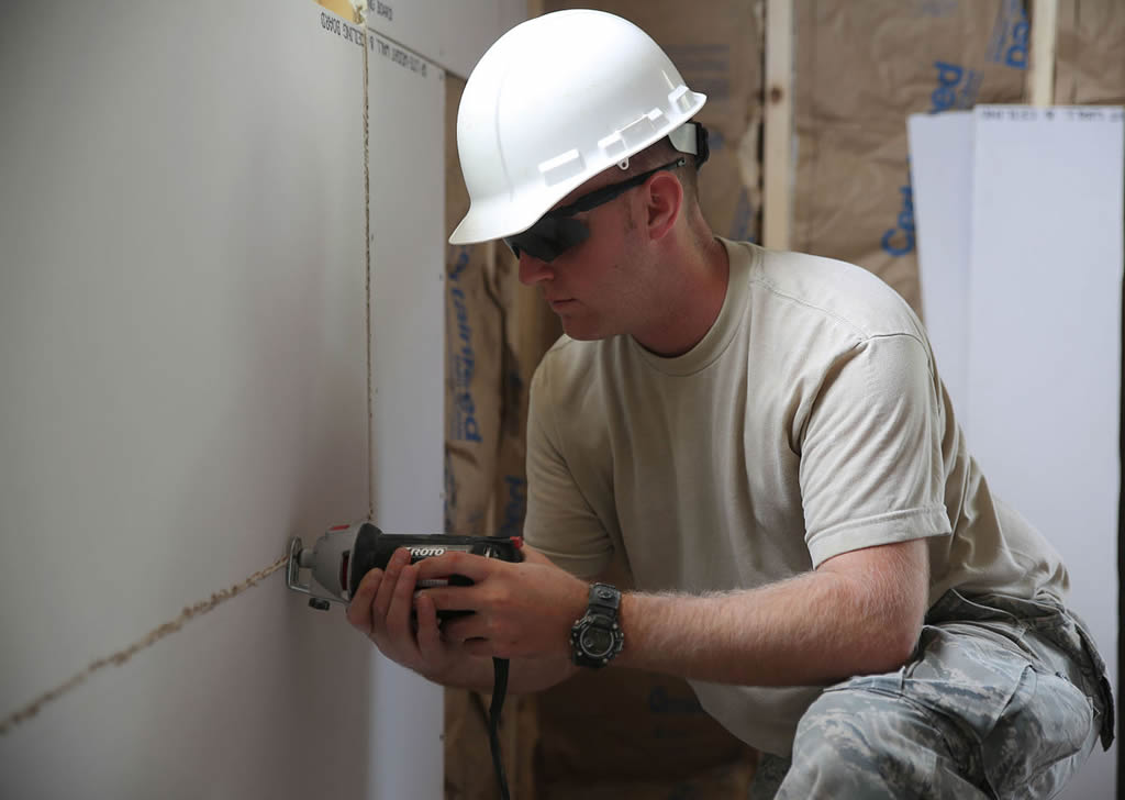 A construction work saws a rectangular hole into drywall